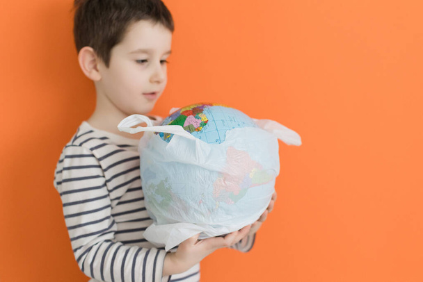 Enfant avec globe dans un sac en plastique sur un fond orange. Concept de problème environnemental, sauver la planète de la pollution - Photo, image