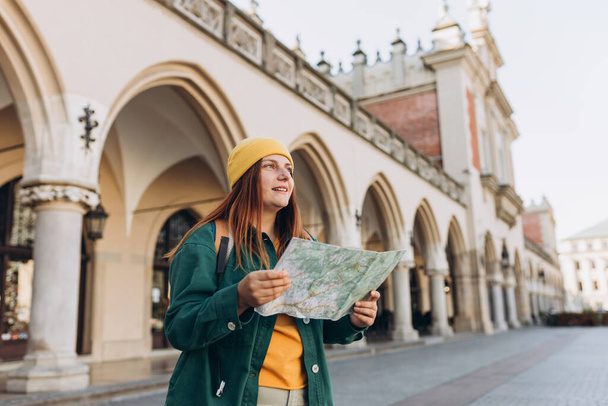 Attraktive junge Touristinnen erkunden die neue Stadt. Rotschopfiges Mädchen mit einer Landkarte aus Papier auf dem Marktplatz in Krakau. Europa bereisen - Foto, Bild