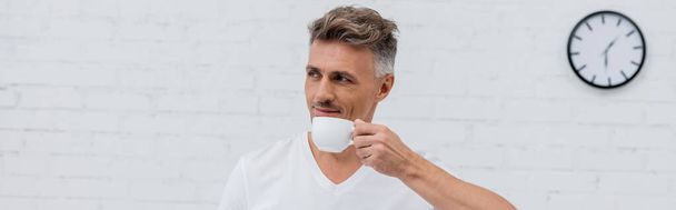 Άντρας σε t-shirt κρατώντας φλιτζάνι καφέ στο σπίτι, πανό  - Φωτογραφία, εικόνα