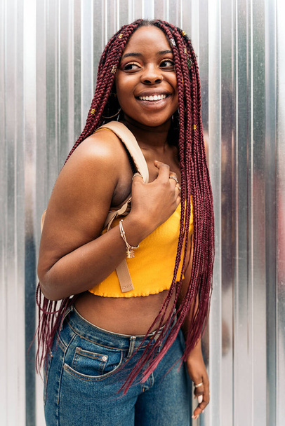 Красивая молодая африканская женщина с косичками смотрит на улицу и улыбается. - Фото, изображение