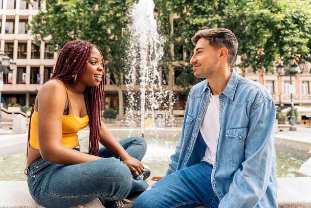Multicultural young friends sitting next to a fountain talking and looking at each other. - Fotografie, Obrázek