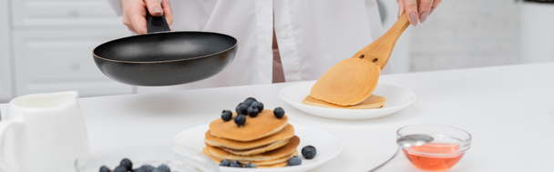 Cropped view of woman in shirt putting pancake on plate near fresh blueberries in kitchen, banner  - Photo, Image