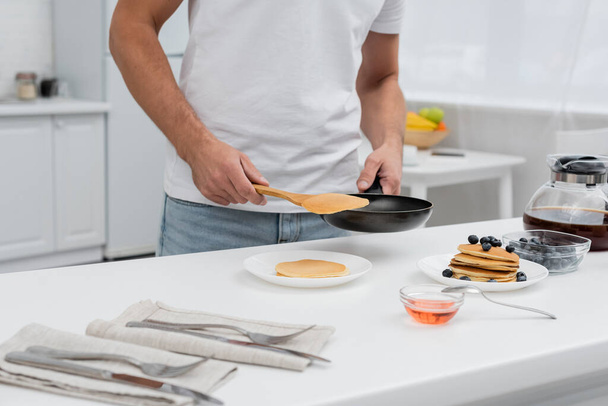 Cropped view of man holding pancake and frying pan near coffee and honey in kitchen  - Foto, Bild