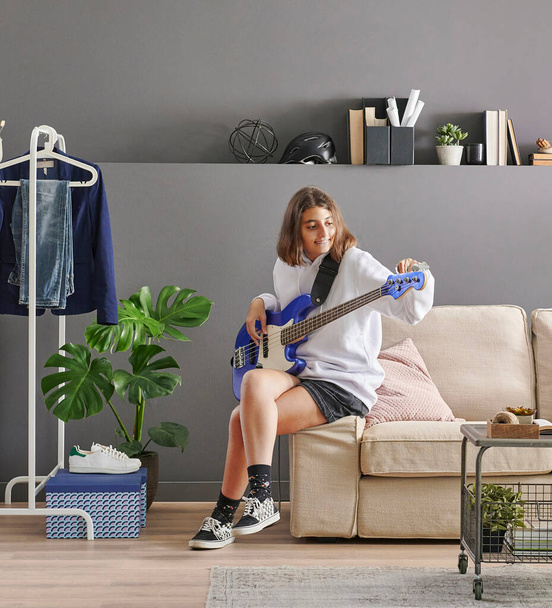 Adolescente tocando una guitarra en el concepto de habitación de pared gris, lavadora y secadora, sofá y estilo de lavandería. - Foto, Imagen