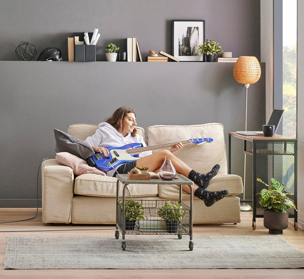 Teenage girl playing a guitar in the grey wall room concept, washing and dry machine, sofa and laundry style. - Fotografie, Obrázek