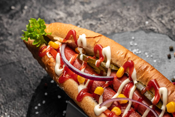 Hot dog, különböző feltétekkel, sötét háttérrel. Étel háttér. gyorsétterem és gyorsétterem koncepció, Utcai ételek. - Fotó, kép