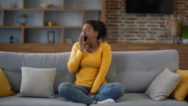 Сезонная апатия. Молодая африканская американка зевает дома на диване, чувствуя усталость и усталость, замедленную съемку, пустое пространство - Кадры, видео