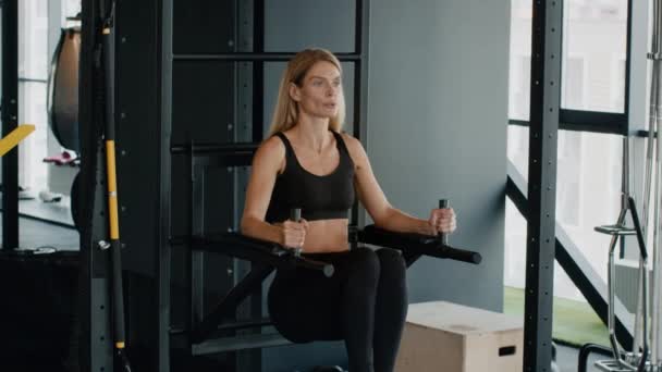 Тренировка по укреплению тела. Активная женщина средних лет тренируется в баре в тренажерном зале, поднимает ноги, тренирует мышцы живота, замедленное движение, свободное пространство - Кадры, видео