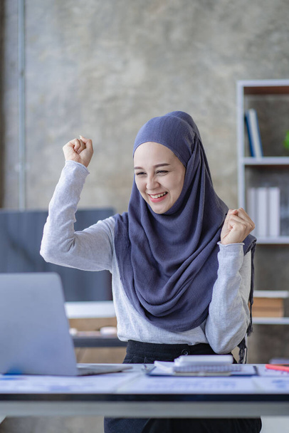 Мусульманская деловая женщина очень взволнована закрытием сделки. Арабская женщина улыбается и работает на ноутбуке с финансовой картой - Фото, изображение