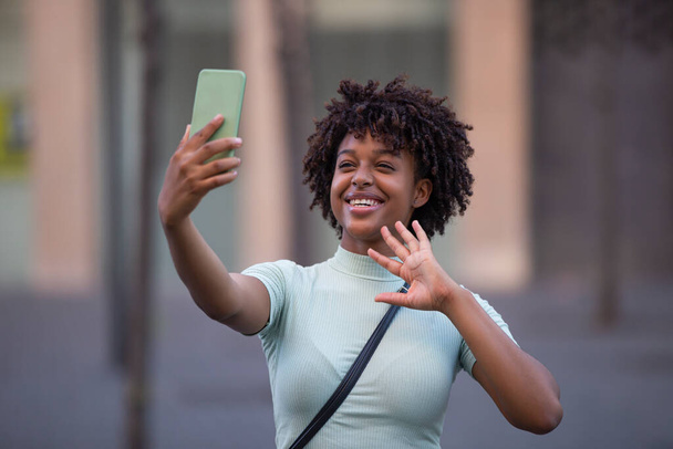 Ευτυχισμένη γυναίκα blogger με αφρο μαλλιά γελώντας, κρατώντας το τηλέφωνο, καταγράφοντας vlog, τραβώντας social media ιστορία ή βιντεοκλήση σε mobile app. - Φωτογραφία, εικόνα
