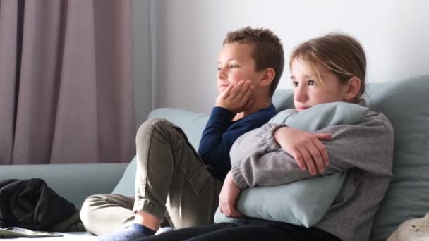 Kinder schauen interessiert fern, wenn sie zu Hause auf dem Sofa sitzen. Interessantes Fernsehen für Kinder. Ein Bruder und eine Schwester im Schulalter ruhen zusammen - Filmmaterial, Video