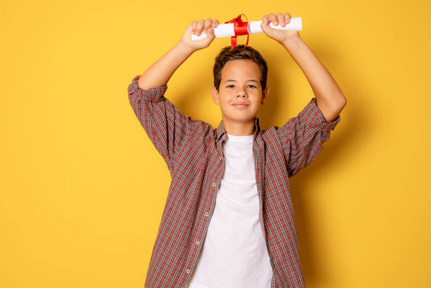 Young little caucasian student kid holding school degree over yellow isolated background. - Photo, Image