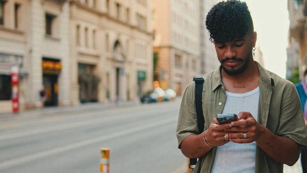 Young smiling man with beard dressed in an olive color shirt uses phone map app on the old city background - Photo, Image