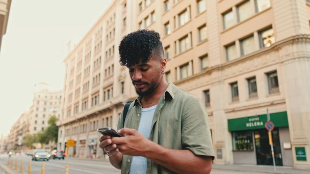 Young smiling man with beard dressed in an olive color shirt uses phone map app on the old city background - Photo, image