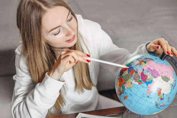 Young blonde woman is studying the globe at home and points her finger at the mainland. Study of geography - Foto, imagen