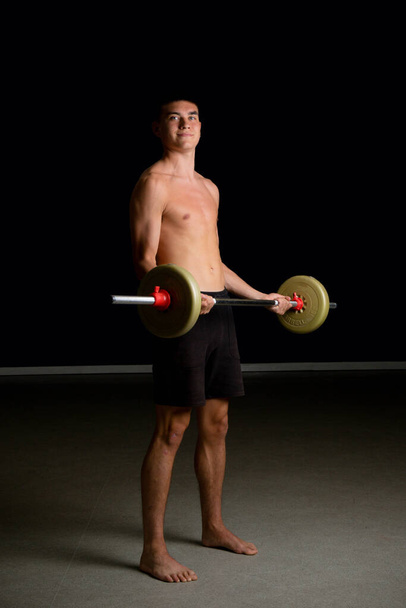 Shirtless 19 year old teenage boy excercsing his bicpes with a barbell - Foto, Imagen