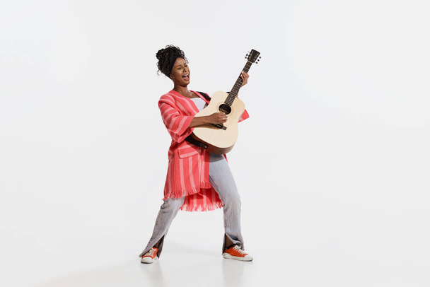 Solo. Stylish african woman wearing vintage style bright clothes playing guitar isolated on white background. Vintage fashion, music, art, emotions, music festival concept. - Photo, Image