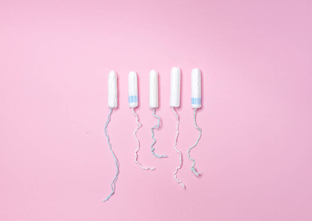 Many sanitary tampons lie in a row on a light pink background. Menstrual cycle and pregnancy. Negative pregnancy test and contraceptives - Photo, Image