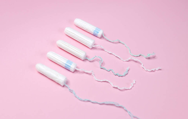 Wiele tamponów sanitarnych leży w rzędzie na jasnoróżowym tle. Cykl menstruacyjny i ciąża. Negatywny test ciążowy i środki antykoncepcyjne - Zdjęcie, obraz
