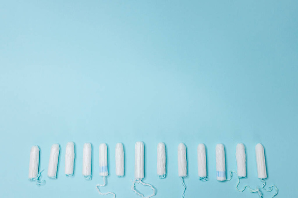 Many sanitary tampons lie in a row on a light blue background. Menstrual cycle and pregnancy. Negative pregnancy test and contraceptives - Photo, Image