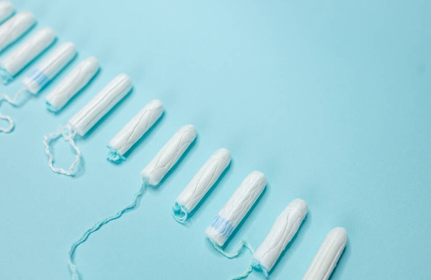 Many sanitary tampons lie in a row on a light blue background. Menstrual cycle and pregnancy. Negative pregnancy test and contraceptives - Фото, зображення