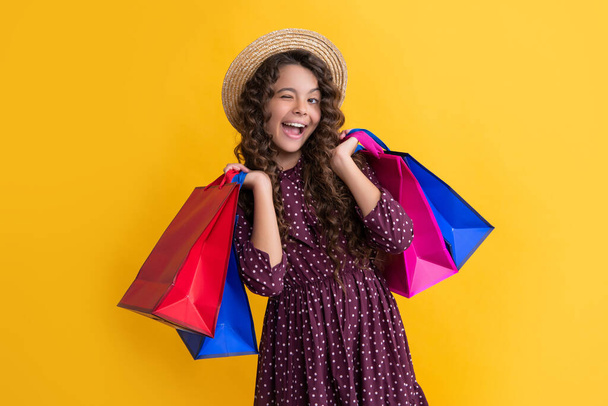 winking girl with curly hair hold shopping bags on yellow background. - Фото, зображення