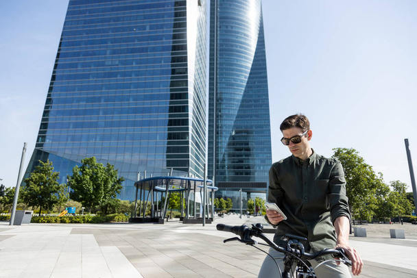 νεαρός επιχειρηματίας οδηγεί e-bike στο δρόμο του προς τον πύργο όπου βρίσκεται το γραφείο του - Φωτογραφία, εικόνα