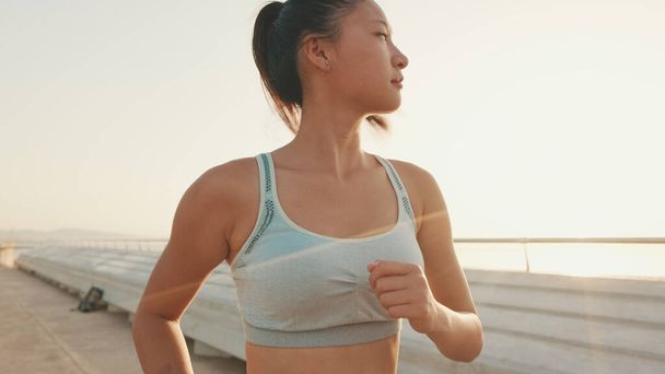 Asian girl in sports top runs along the promenade at morning time - 写真・画像
