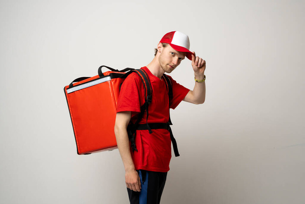 Side view courier guy in red uniform with a thermo blackpack on white background - Foto, immagini