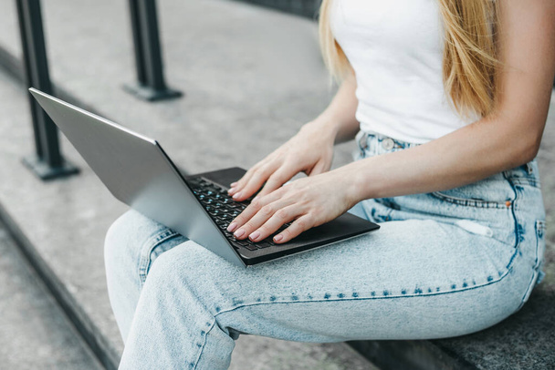 Dizüstü bilgisayarı olan öğrenci kız üniversite binasının arka planında oturuyor. - Fotoğraf, Görsel