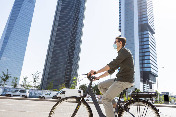 молодой бизнесмен едет на электронном велосипеде по пути к башне, где расположен его офис - Фото, изображение