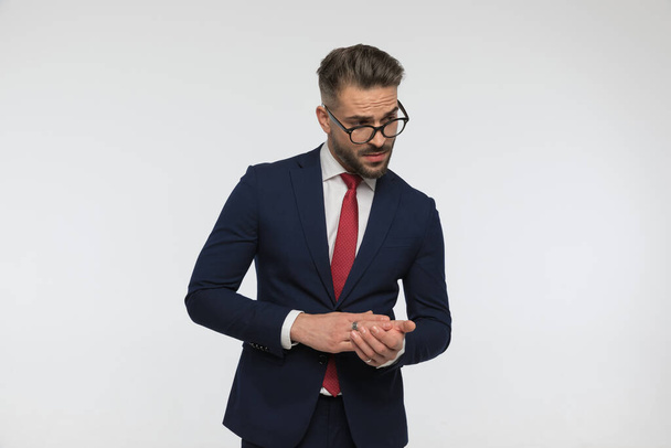 sexy uomo con gli occhiali indossa abito elegante e palme sfregamento mentre guardando altrove e di essere fresco su sfondo bianco in studio - Foto, immagini