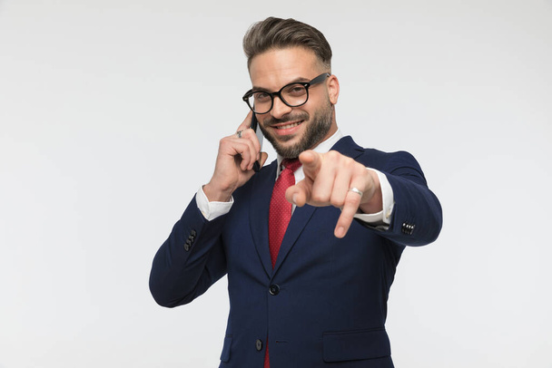 ritratto di un uomo d'affari sorridente con gli occhiali che fa conversazione e punta il dito davanti allo sfondo bianco in studio - Foto, immagini