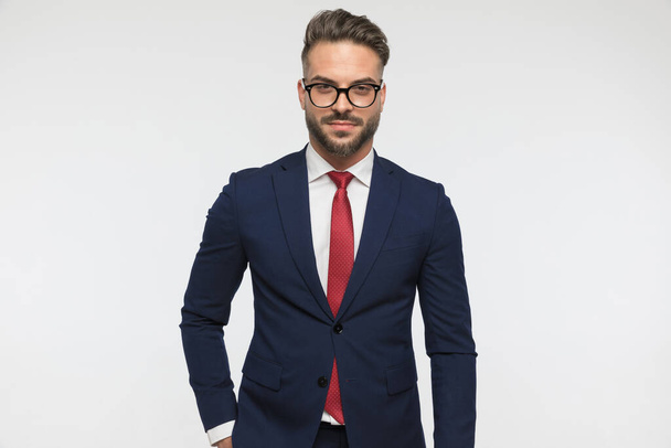 portret przystojnego mężczyzny w okularach trzymającego rękę w kieszeni i mającego pewność siebie przed białym tłem w studio - Zdjęcie, obraz