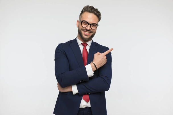 funny young guy with red tie and elegant suit laughing and pointing fingers to side on white background in studio - Foto, afbeelding