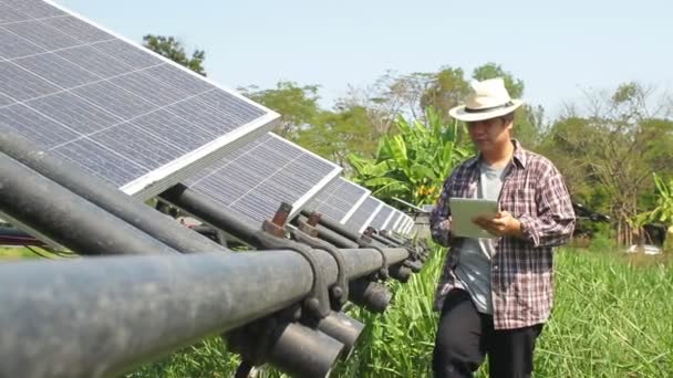 Asiatischer männlicher Bauer, der eine Tablette in der Hand hält, um die Solarzelle zur Umwandlung von Sonnenenergie in Elektrizität zu steuern. Moderne landwirtschaftliche Konzepte. Einsatz moderner Technologie - Filmmaterial, Video