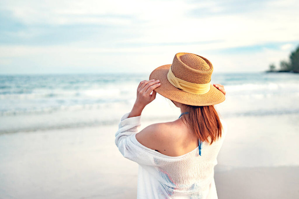 Концепция летнего пляжного отдыха, молодая женщина в шляпе, расслабляясь с поднятыми руками, наслаждаясь видом на пляжный океан в жаркий летний день, копирование пространства. - Фото, изображение