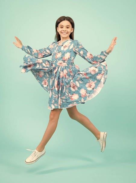Full length cheerful teenager kid jump enjoy rejoice win isolated on blue background. Small child girl in summer dress jumping. Excited teenager, amazed and cheerful emotions - 写真・画像