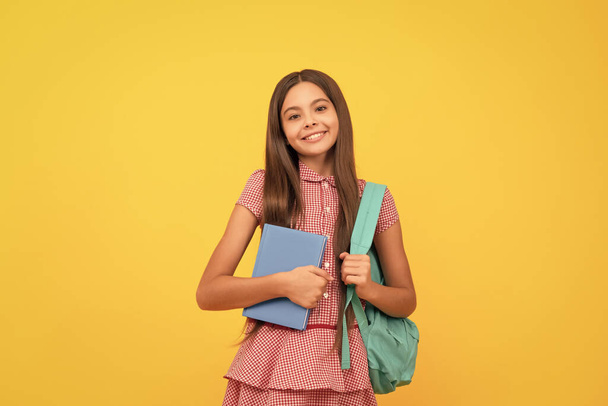 september 1. happy childhood. child with school bag. cheerful teen girl carry backpack. back to school. knowledge day. concept of education. kid with workbook on yellow background. - Фото, изображение