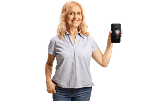 Casual mature woman showing a smartphone with a broken screen isolated on white background - Foto, Imagem