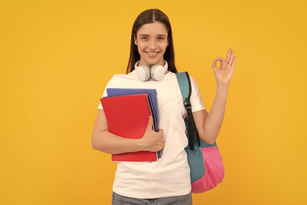 back to school. modern education concept. ok gesture. happy student hold notebook. girl holding notebook on yellow background. private teacher with copybooks and headphones. - Foto, imagen