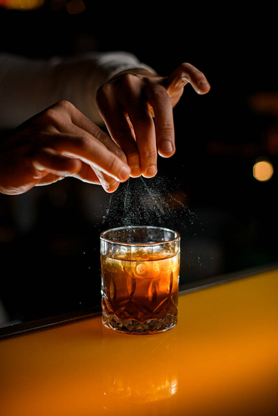 great view on male fingers holding orange zest and splashing on an old-fashioned glass with alcohol cocktail - Φωτογραφία, εικόνα
