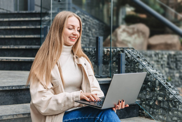 Happy student girl sitting on stairs near office center with laptop smiling and studying. online education - Foto, Bild