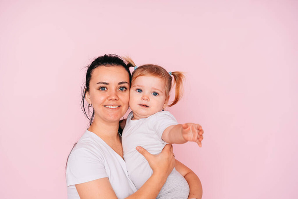 Eine glückliche Mutter mit ihrem Baby auf rosa Hintergrund. Umarmungen von Mutter und Baby auf rosa Hintergrund. Eine liebevolle Familie. Das Konzept der Familie. - Foto, Bild
