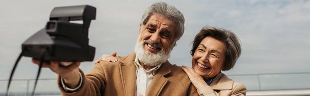 happy senior man taking selfie with cheerful wife on vintage camera, banner - Photo, Image