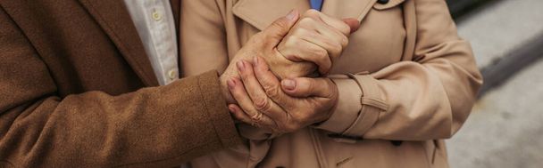 cropped view of senior man holding hand of wife in trench coat outside, banner - Foto, imagen