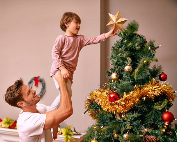 Είναι οικογενειακή παράδοση... ένας πατέρας να σηκώνει το γιο του για να βάλει το αστέρι στο χριστουγεννιάτικο δέντρο. - Φωτογραφία, εικόνα