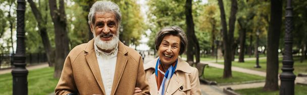 happy senior woman and stylish man in coats smiling in green park, banner - Foto, Imagem