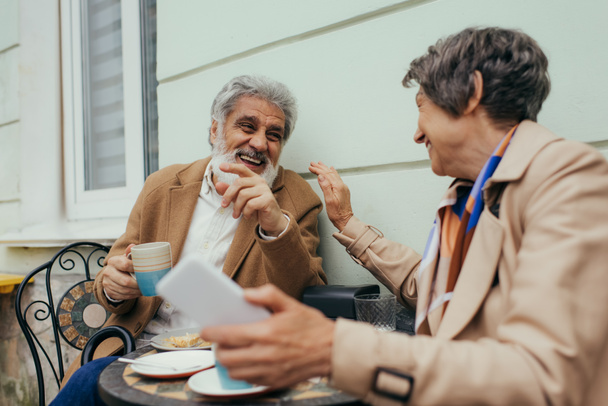 alegre pareja de ancianos riendo durante el almuerzo en la terraza de la cafetería  - Foto, Imagen