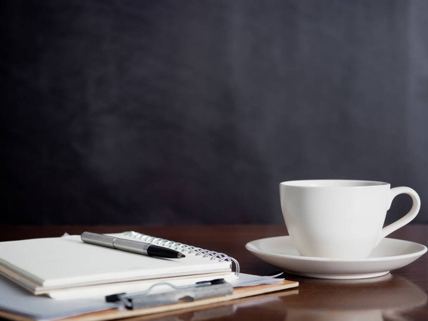 Kannettava kynä ja valkoinen kahvikuppi puupöydällä tumma tausta - Valokuva, kuva